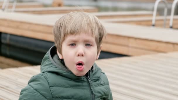 Kleine jongen buiten zitten aan de rivier, met een hoest — Stockvideo