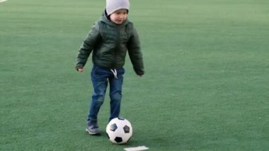 Genç çocuk yeşil çimlerde futbol topunu tekmeliyor.