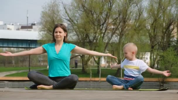 Egy nő a fiával jógázik a tónál, a szabadban. — Stock videók