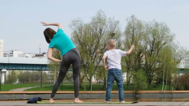 Жінка з сином робить йогу біля ставка, на відкритому повітрі — стокове відео