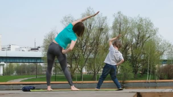 Vrouw met haar zoon doet yoga bij de vijver, buiten — Stockvideo