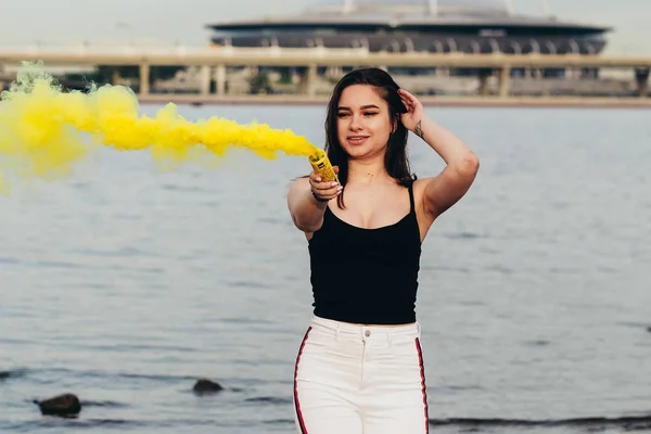 Conceito de juventude e alegria. Menina bonita feliz no litoral segurar uma luz até bombas de fumaça coloridas. Adolescentes . — Fotografia de Stock