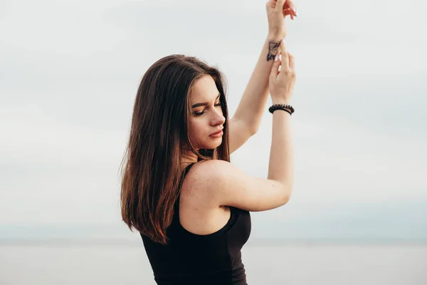 Youth and joy. Beautiful young girl with dark hair spreading arms up at the seaside. Morning. — Stock Photo, Image