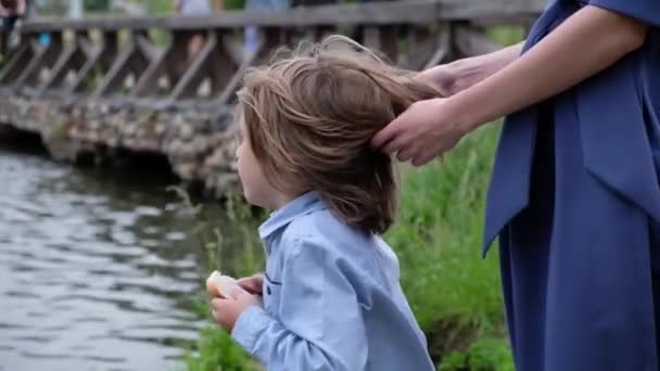 Un niño alimentando patos junto al río. Madre acariciando el pelo de los niños. Verano al aire libre. De cerca. — Vídeos de Stock