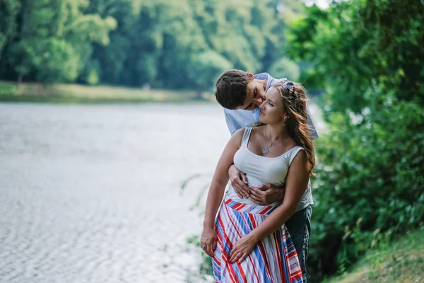 Ungt kärleksfullt par som kramar, omfamnar varandra ömt på vacker plats vid floden — Stockfoto