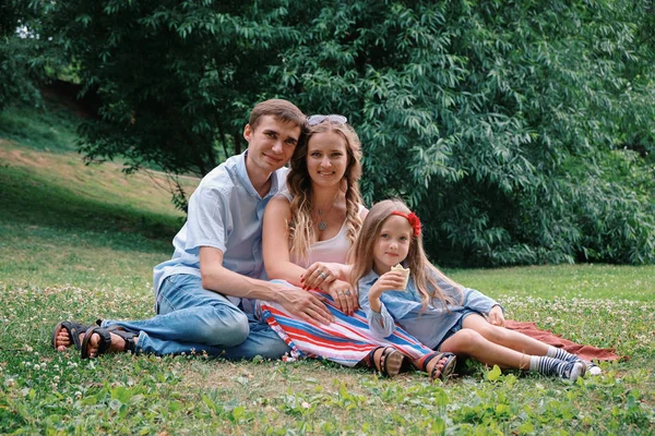 Concetto di famiglia: donna, uomo e figlia seduti nel parco. Estate all'aria aperta — Foto Stock