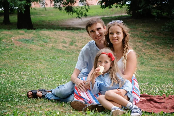 Family concept: woman, man and daughter sitting in the park. Summer outdoors