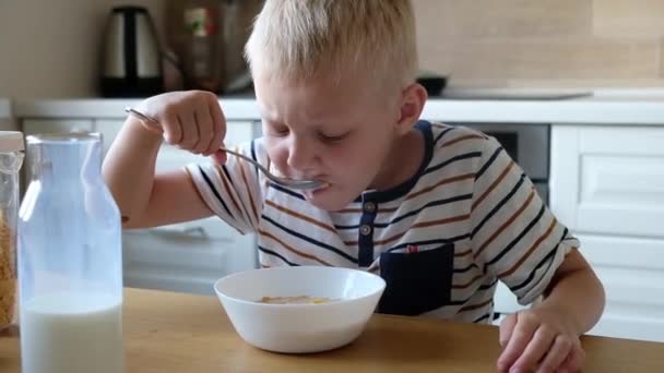 かわいい男の子4歳は、自宅のテーブルでミルクと朝食コーンフレークを持っています. — ストック動画