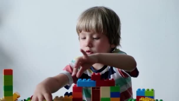 Schattige jongen 4 jaar oud spelen met kleurrijke plastic speelgoed bakstenen aan de tafel thuis. — Stockvideo