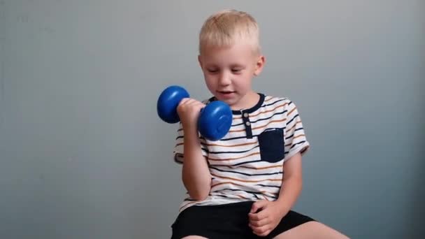 Симпатичный мальчик 6 лет, делает упражнения с гантели на сером фоне — стоковое видео