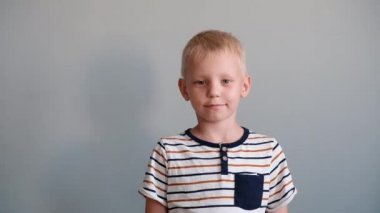 Sevimli çocuk 6 yaşında kameraya bakarak ve gülümseyerek oynuyor. Gri arka plan