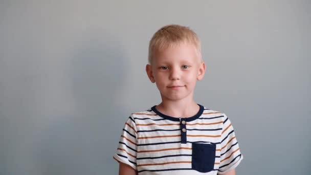 Schattige jongen 6 jaar oud spelen kijken naar camera en glimlachend. Grijze achtergrond — Stockvideo