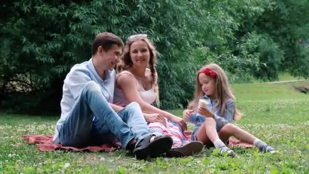 Сімейна концепція: жінка, чоловік і дочка сидять у парку. Літо на відкритому повітрі — стокове відео