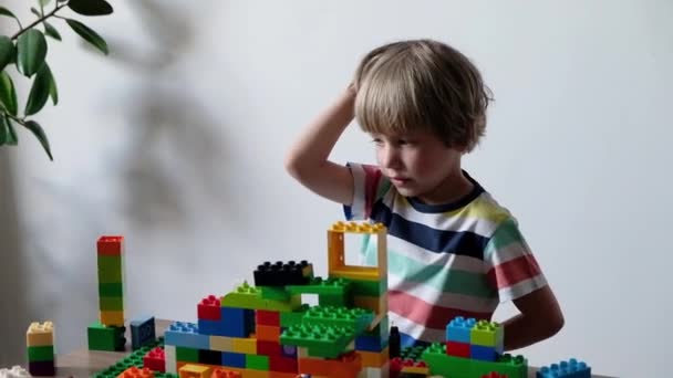 Süßer Junge 4 Jahre alt spielt mit bunten Plastikspielzeugsteinen am heimischen Tisch. — Stockvideo