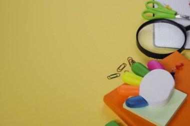 Geri okul kavramı, sarı arka plan üzerinde çeşitli okul malzemeleri ve kırtasiye ile yaratıcı düzeni.
