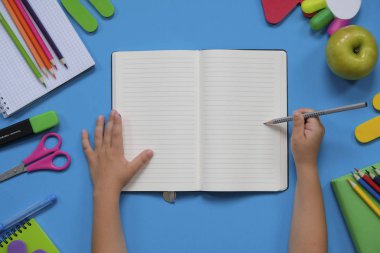 Geri okul kavramı, mavi arka plan üzerinde çeşitli okul malzemeleri ve kırtasiye ile yaratıcı düzeni. Çocuk elleri. Düz döşeme stil kompozisyonu, yukarıdan görünüm