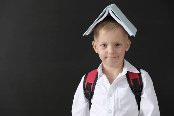 Je retourne à l'école. Petit garçon drôle au tableau noir. Enfant de l'école primaire avec un livre sur la tête. Concept d'éducation . — Photo