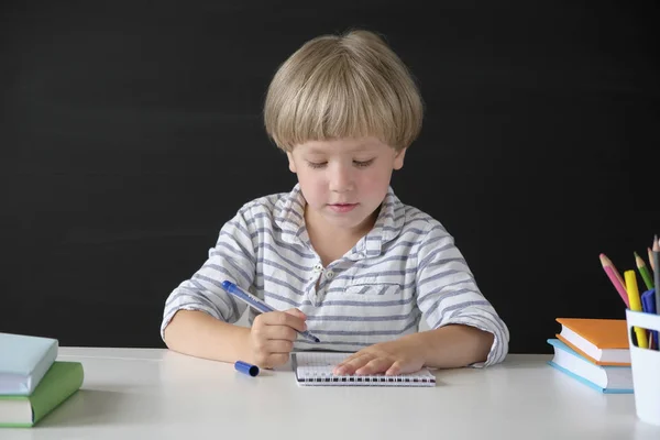 Terug naar school. Schattige kleine jongen zittend aan de tafel op Blackboard backgrpund. Kind van de basisschool. Education concept. — Stockfoto