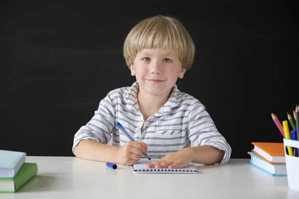 De vuelta a la escuela. Lindo niño sentado en la mesa en la pizarra backgrpund. Niño de la escuela primaria. Concepto educativo . — Foto de Stock