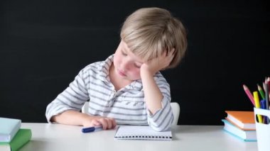 Sevimli küçük çocuk okurken sıkılıyor. Tahtadaki ilkokuldan bir çocuk. Eğitim kavramı.