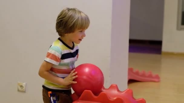 De jongen speelt Bowlen. Hij rolt de bal op het pad van een speciale Kinder heuvel — Stockvideo