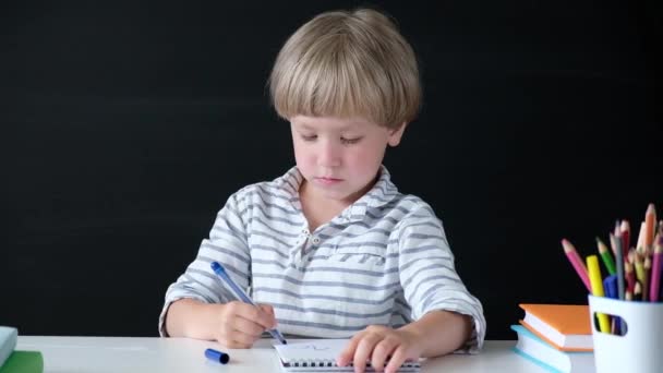 귀여운 소년 테이블에 그리기. 초등학교 아이. 교육 개념입니다. 학교로 돌아가기. — 비디오