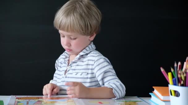 Cute Little Boy siedzi przy stole i czytania. Dziecko z szkoły podstawowej. Koncepcja edukacyjna. Powrót do szkoły. — Wideo stockowe