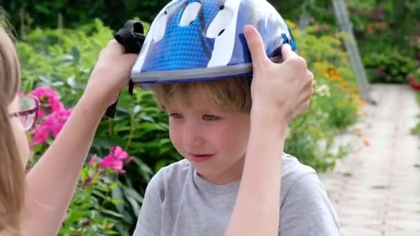 Anne, oğlunun şehir parkında güvenli bir şekilde bisiklete binmesi için kask takmasına yardım ediyor. — Stok video