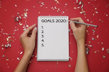 Metin hedefleri 2020 ve şenlikli kırmızı arka planda kalem ile kadın elleri ile defter