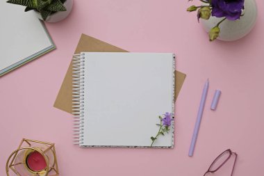 Boş not defteri, çiçekler ve kalem tasarımınız için maket olarak. Pembe arka plan, düz döşeme stili.