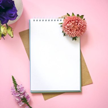 Tasarım için mockup olarak boş not defteri ve çiçekler. Pembe arka plan, düz döşeme stili.