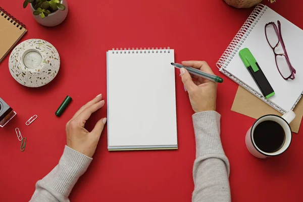 Kadın elleri tasarım için mockup olarak kalem ve not defteri tutarak. Kırmızı arka plan, düz döşeme tarzı. Yukarıdan görüntüle.
