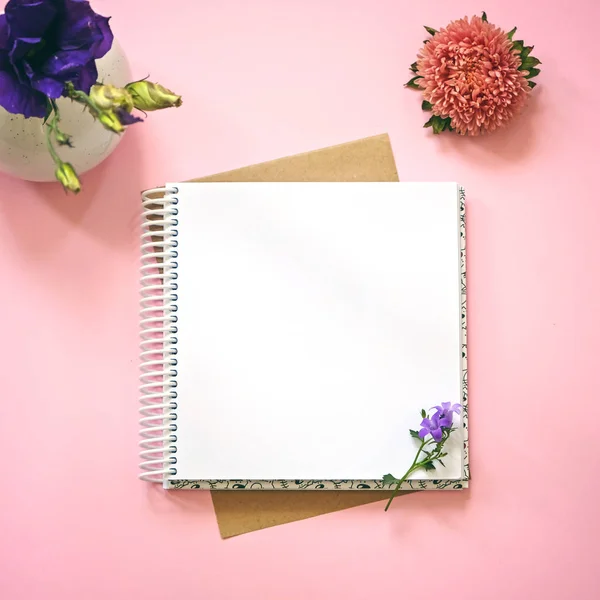 Blank notepad and flowers as mockup for your design. Pink background, flat lay style.