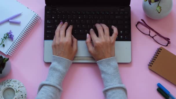 Womans hands working on laptop on modern pink background, workspace, view from above — Stock Video