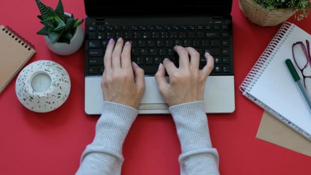 Женские руки, работающие на ноутбуке на современном красном столе, вид сверху — стоковое видео