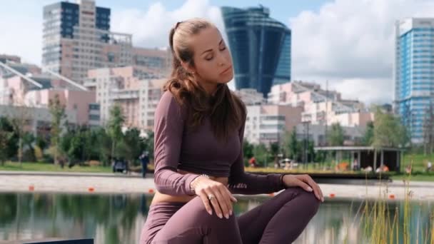 Jovem mulher senta-se em pose de ioga com a cidade no fundo. Relaxar e conceito de liberdade . — Vídeo de Stock