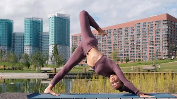 Genç kadın arka planda şehir ile yoga egzersizleri yapıyor. eka pada adho mukha svanasana — Stok video