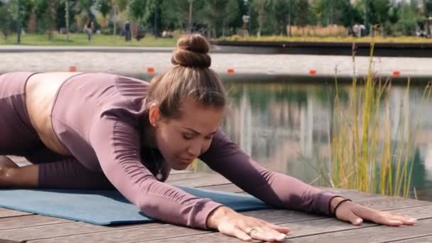 Jonge vrouw doet yoga oefeningen met stad op achtergrond. Eka Pada rajakapotasana. Duif pose — Stockvideo