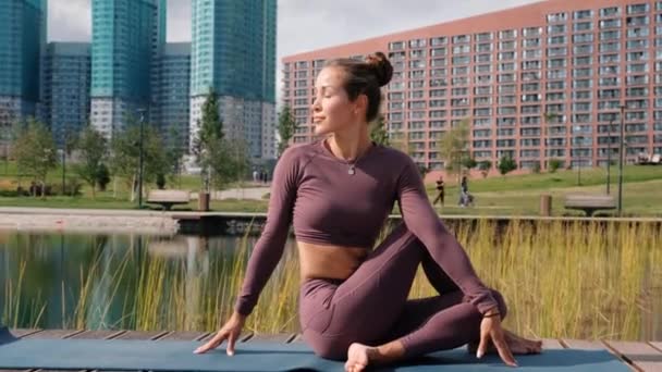 Junge Frau macht Yoga-Übungen mit der Stadt im Hintergrund. Schrauben-Pose, ardha matsyendrasana — Stockvideo