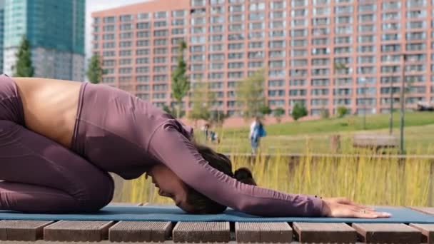 Mujer joven haciendo ejercicios de yoga con la ciudad en el fondo. Balasana — Vídeos de Stock