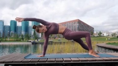 Genç kadın arka planda şehir ile yoga egzersizleri yapıyor. Denge pozu. Çamatkarasana