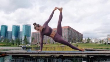 Genç kadın arka planda şehir ile yoga egzersizleri yapıyor. Güzel denge poz