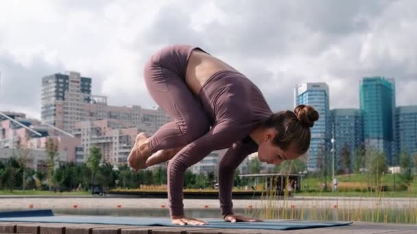 Young woman doing yoga exercises with city on background. Bakasana — Stock Video