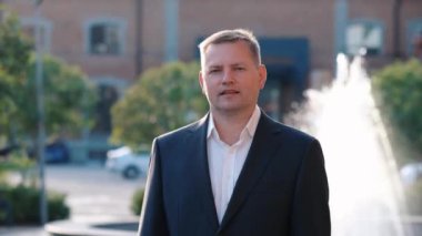 Kendine güvenen işadamı kameraya bakıyor ve gülümsüyor, açık havada