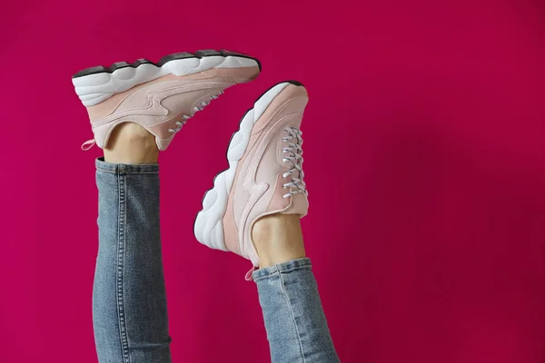 Pembe bir arka plan üzerinde markasız modern sportif ayakkabı kadın ayakları.