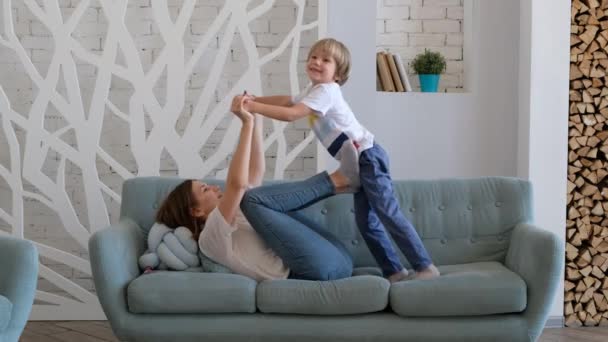 快乐的妈妈正在和她的儿子玩耍，把他像飞机一样举起来。孩子和妈妈玩得很开心。室内 — 图库视频影像