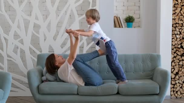 Mãe alegre está brincando com seu filho levantando-o como um avião. Criança se divertindo com a mãe. Interior — Vídeo de Stock