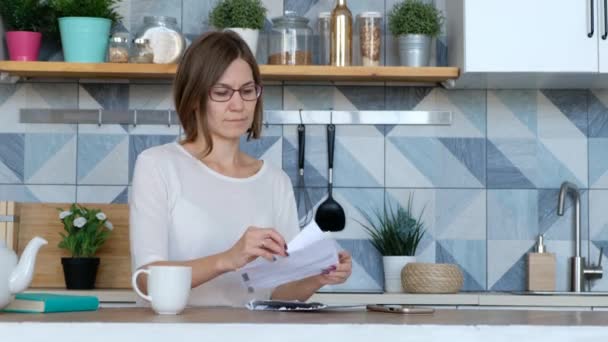 Stress wegen Rechnungen. Überraschte und verunsicherte Frau beim Betrachten ihrer finanziellen Schulden in der Küche. — Stockvideo