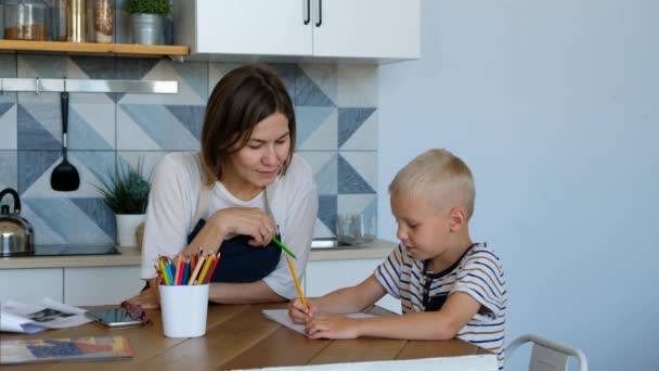 Madre ayudar a su hijo a hacer la tarea en la sala de cocina. Personas con familia, estilo de vida y concepto de educación . — Vídeos de Stock