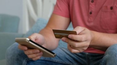Genç beyaz adam oturma odasında kredi kartı ile online alışveriş için akıllı telefon kullanarak. .